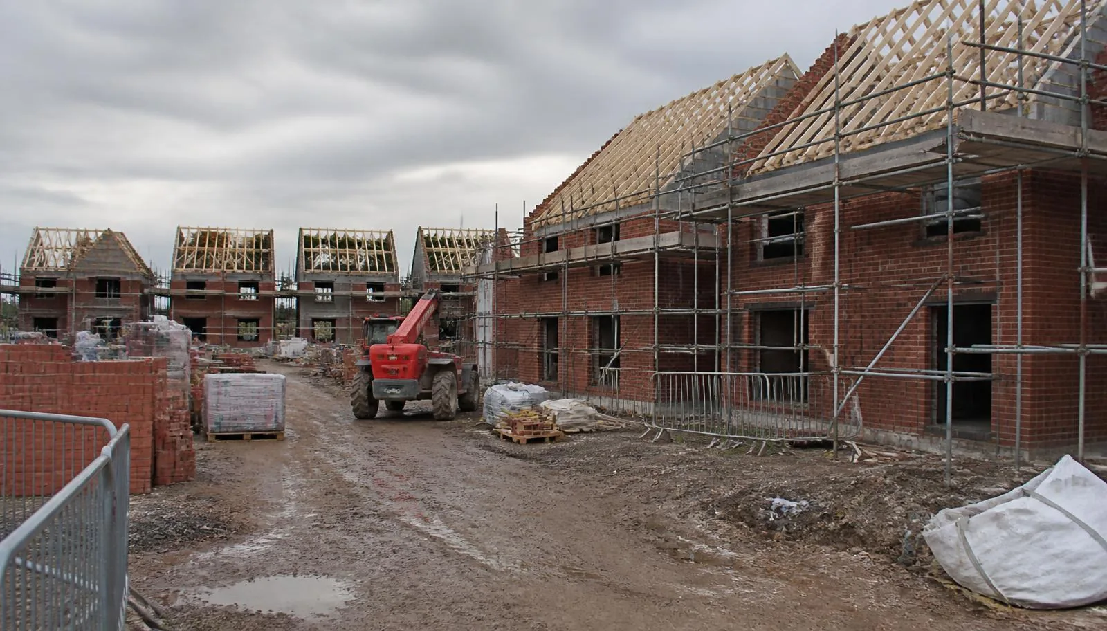 Part-built brick houses with scaffolding and roof trusses on an active UK residential new-build development.